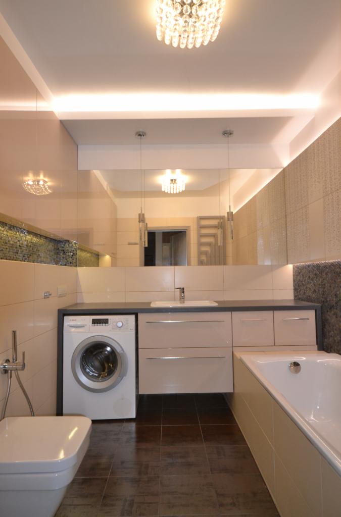 Nowoczesna łazienka z pralką w zabudowie, lustrem na całą ścianę i ozdobnym oświetleniem sufitowym.