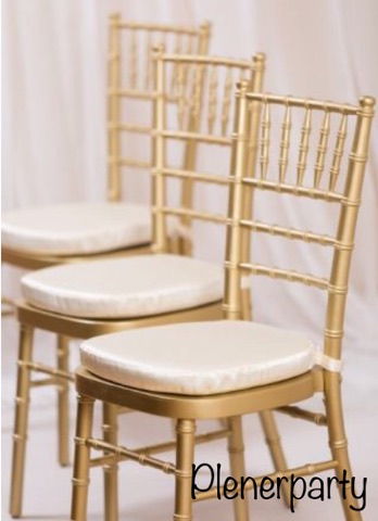 Trzy złote krzesła Chiavari z kremowymi poduszkami ustawione w rzędzie na tle białej zasłony.