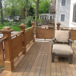 Wykończony taras z drewnianą balustradą z dekoracyjnymi słupkami i krzesłem z poduszkami w Ełku, widok na ogród i fragment domu.