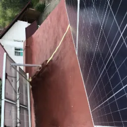 Czerwony, płaski dach budynku z panelami słonecznymi, zabezpieczony żółtą pianą uszczelniającą, widok z góry.