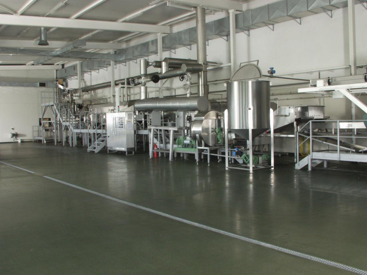 Wnętrze hali produkcyjnej z linią technologiczną wykonaną ze stali nierdzewnej, widoczne zbiorniki, rury, schody i panele sterowania.