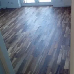 Ułożona podłoga z paneli drewnopodobnych w nowym mieszkaniu, widok na okno balkonowe i grzejnik, jasne ściany.