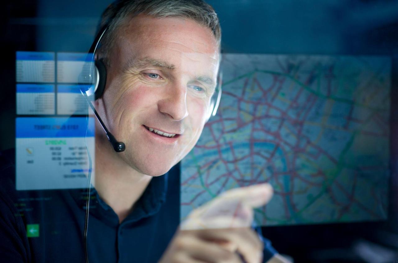Dyspozytor w słuchawkach wskazuje palcem na interaktywną mapę z trasami transportu na ekranie.