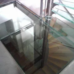 Szklana podłoga z widocznymi schodami spiralnymi pod spodem, mocowana metalowymi elementami.