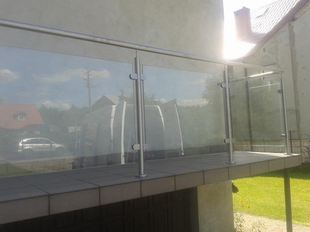 Szklana balustrada balkonowa z elementami ze stali nierdzewnej, widoczna z zewnątrz, odbijająca otoczenie w szybach.