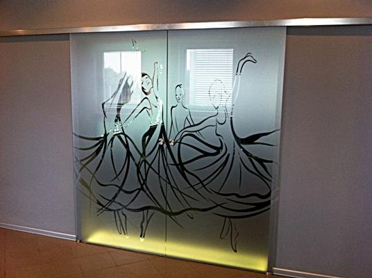 Szklane drzwi przesuwne z matowym wykończeniem i czarnym, stylizowanym motywem trzech tańczących postaci w sukniach.