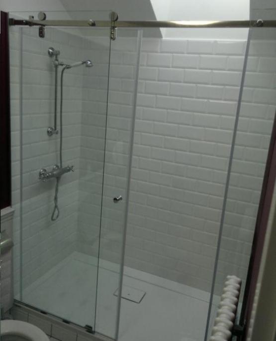 Kabina prysznicowa z przesuwnymi szklanymi drzwiami na szynie, wykończona białymi płytkami typu metro, widoczny odpływ liniowy w brodziku.