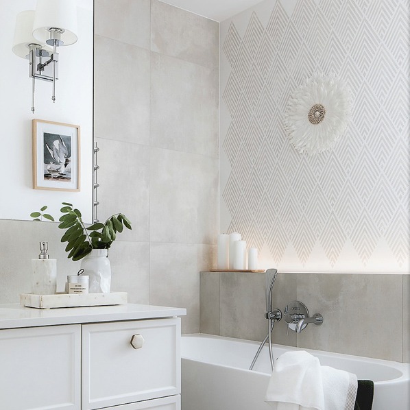 Jasna łazienka w Warszawie z geometrycznym wzorem na ścianie, białymi świecami i dekoracyjnym pióropuszem nad wanną.