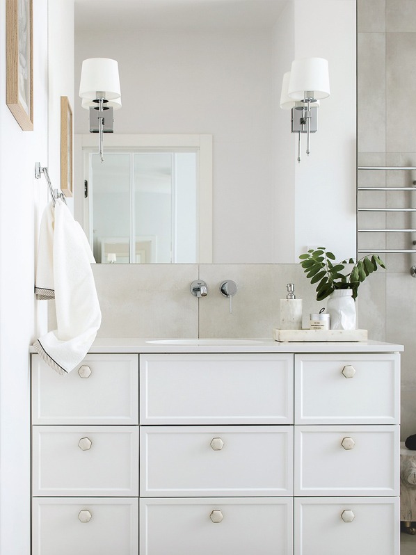 Jasna łazienka z białą szafką pod umywalką z sześciokątnymi uchwytami, chromowaną armaturą i minimalistycznymi kinkietami.