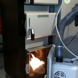 Nowoczesny piec na paliwo stałe marki Kotłostal z otwartymi drzwiczkami paleniska, ukazującymi płomienie. Widoczne oznaczenia 'WYCZYSTKA' oraz naklejka z klasą energetyczną 5.