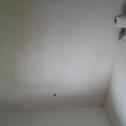 Świeżo otynkowany, jasny sufit z widocznym gniazdkiem elektrycznym i śladami po pracy, z niedoskonałościami i śladami farby na ścianach.