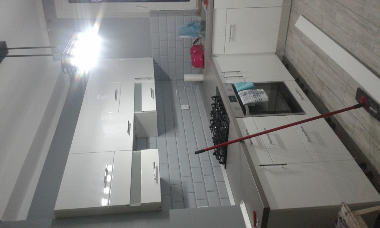 Nowoczesna, jasna kuchnia z białymi szafkami na tle szarych, prostokątnych płytek, widok z góry, z mopem opartym o blat, sugerującym sprzątanie po remoncie.