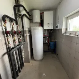 Kotłownia z zamontowaną pompą ciepła Panasonic, zasobnikiem ciepłej wody, grupą pompową z czterema obiegami, instalacją hydrauliczną z rurami w izolacji termicznej i niewielkim zbiornikiem...