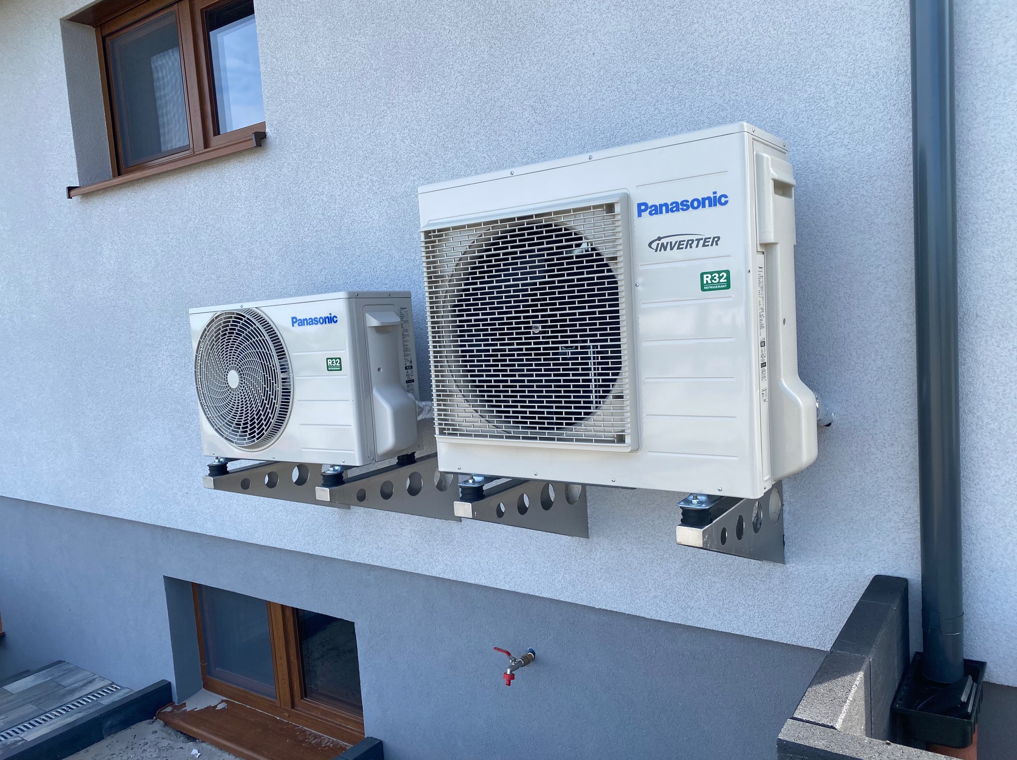 Dwa białe, zamontowane na metalowych wspornikach agregaty klimatyzacyjne Panasonic Inverter R32 na elewacji budynku z widocznymi oknami.