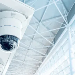 Kamera monitoringu kopułkowa zamontowana pod sufitem, widoczny system przeciwpożarowy i konstrukcja sufitu w tle.