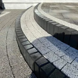 Ułożona nawierzchnia z jasnoszarej kostki brukowej oddzielona ciemnoszarym obrzeżem, tworząca łukowaty wzór na podjeździe.