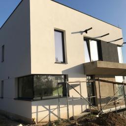 GPM Constructions - Nowoczesny dom jednorodzinny w trakcie tynkowania elewacji, widoczne rusztowania i fragment krajobrazu w tle.