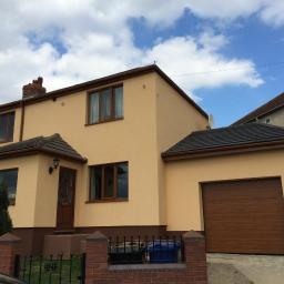 GPM Constructions - Dom jednorodzinny z ocieploną i otynkowaną elewacją w odcieniach beżu i brązu, z garażem wbudowanym i zadbanym otoczeniem.