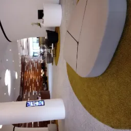 Nowoczesne wnętrze biurowe z białymi kolumnami, designerskimi meblami wypoczynkowymi i dekoracyjną ścianą z drewnianymi elementami, oświetlone punktowymi lampami sufitowymi.