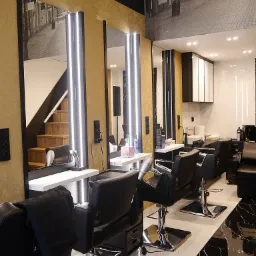 Wnętrze salonu fryzjerskiego w Krakowie, z fotelami fryzjerskimi, lustrami z podświetleniem LED, złotymi ścianami i fototapetą z motywem ulicy Starowiślnej.