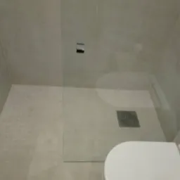 Nowoczesna kabina prysznicowa walk-in z odpływem liniowym, wykończona płytkami w odcieniach szarości, z widoczną częścią toalety z przodu.