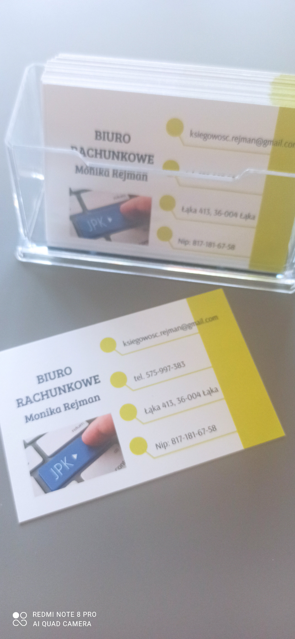Wizytówki biura rachunkowego Monika Rejman w przezroczystym podajniku, z adresem, NIP i mailem. Na wizytówce grafika klawisza JPK.