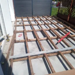 Konstrukcja pod taras w Sosnowcu. Drewniany szkielet z legarów, poziomica, wkrętarka i skrzynka narzędziowa w tle. Widok z góry na plac budowy.