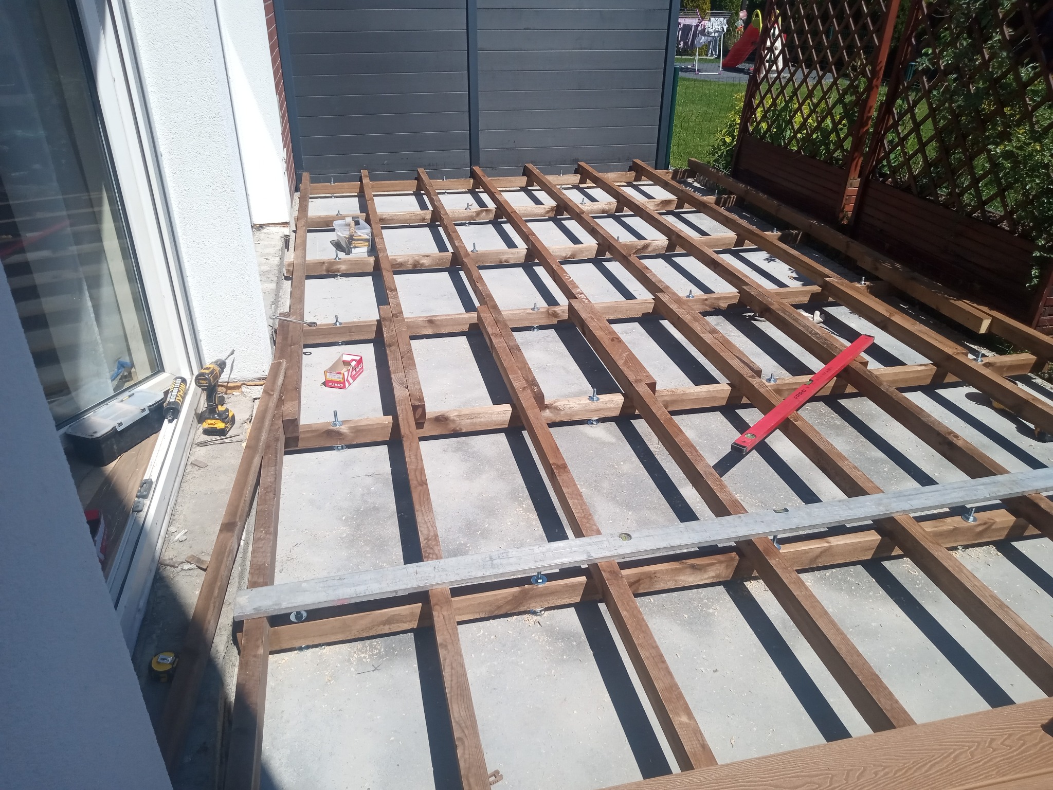 Konstrukcja pod taras w Sosnowcu. Drewniany szkielet z legarów, poziomica, wkrętarka i skrzynka narzędziowa w tle. Widok z góry na plac budowy.