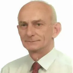 Portret starszego mężczyzny w białej koszuli i czerwonym krawacie na jasnym tle. Widoczne zmarszczki i łysina. Ujęcie od ramion w górę, z delikatnym uśmiechem.