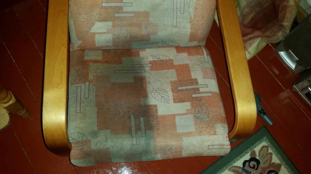 Fotel z drewnianymi podłokietnikami i wzorzystą tapicerką, w trakcie czyszczenia - widoczny fragment mokrej powierzchni po prawej stronie.