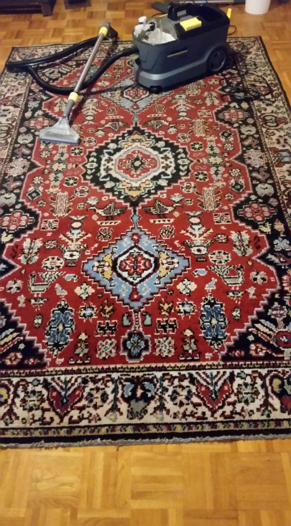 Czerwony, wzorzysty dywan orientalny podczas czyszczenia odkurzaczem piorącym Karcher. Widoczne ślady wilgoci po praniu.