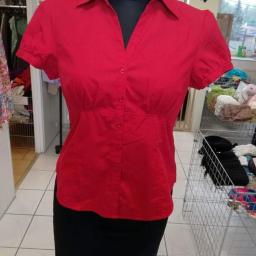 Fabryka mody - Czerwona bluzka z krótkim rękawem i czarna spódnica na manekinie w sklepie z odzieżą, widoczne wieszaki z ubraniami w tle.