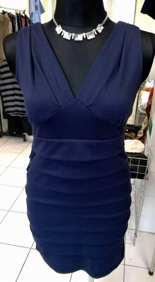 Granatowa, dopasowana sukienka z dekoltem w serek i poziomymi marszczeniami na manekinie, uzupełniona srebrnym naszyjnikiem z geometrycznymi elementami.