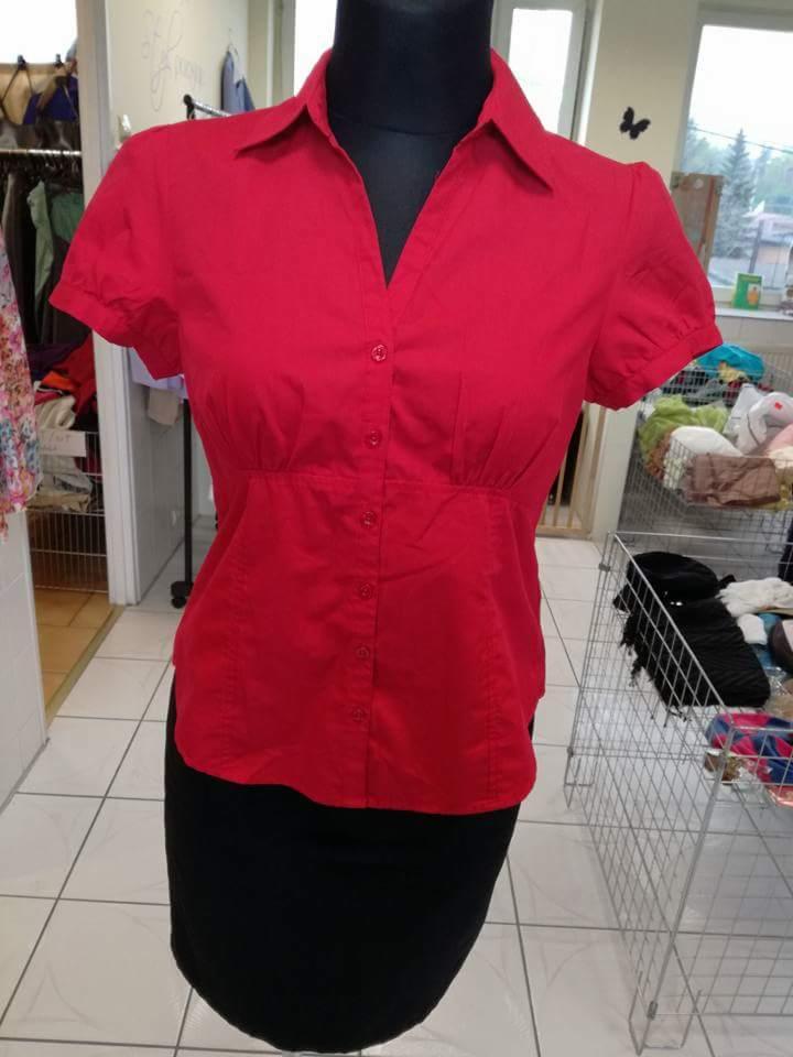 Czerwona bluzka z krótkim rękawem i czarna spódnica na manekinie w sklepie z odzieżą, widoczne wieszaki z ubraniami w tle.