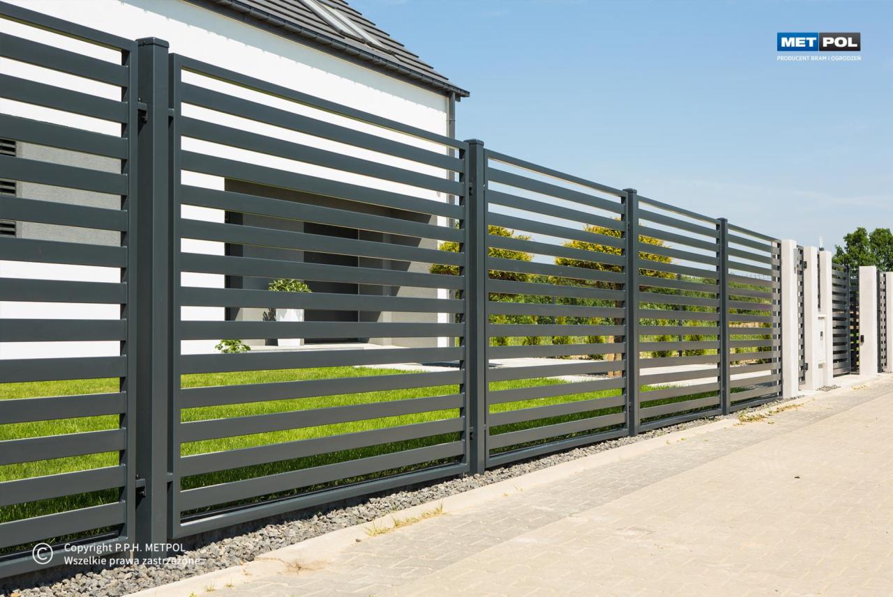Nowoczesne, poziome przęsła w kolorze grafitowym tworzą minimalistyczne ogrodzenie posesji. Widoczny fragment domu z jasną elewacją i zielony trawnik.