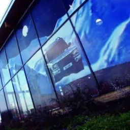 Grafika wielkoformatowa na szklanej fasadzie budynku przedstawiająca samochód terenowy na tle górskiego krajobrazu.