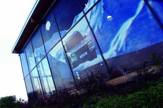 Grafika wielkoformatowa na szklanej fasadzie budynku przedstawiająca samochód terenowy na tle górskiego krajobrazu.