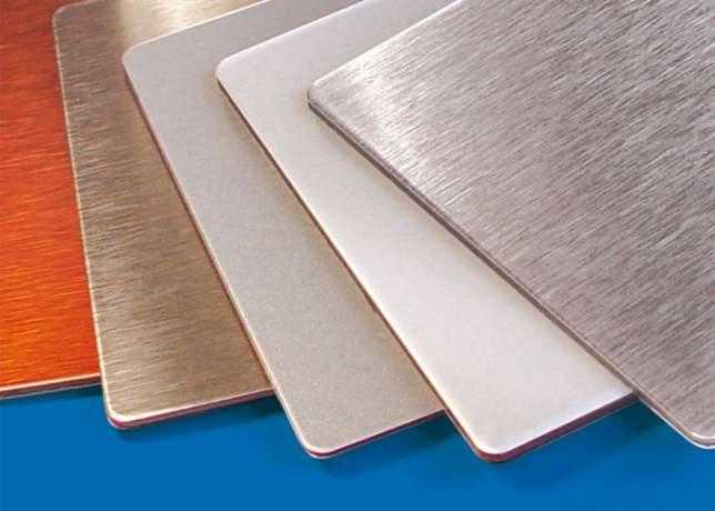 Próbki różnokolorowych, metalicznych płyt kompozytowych z efektem szczotkowanego aluminium, ułożone pod kątem na niebieskim tle.