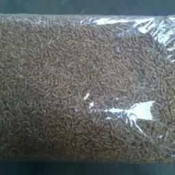 Przezroczysty worek wypełniony brązowymi granulkami biomasy drzewnej, widoczne nierównomierne oświetlenie i szary beton w tle.