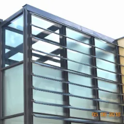 Szklana fasada budynku biurowego z żaluzjami zewnętrznymi, widok z dołu na jasnym tle nieba.