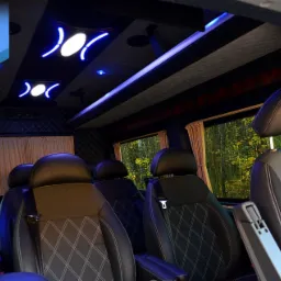 Wnętrze luksusowego busa Peugeot Boxer VIP 8+1 z czarną, pikowaną tapicerką, oświetleniem LED w kolorze niebieskim i widokiem na las za oknem.