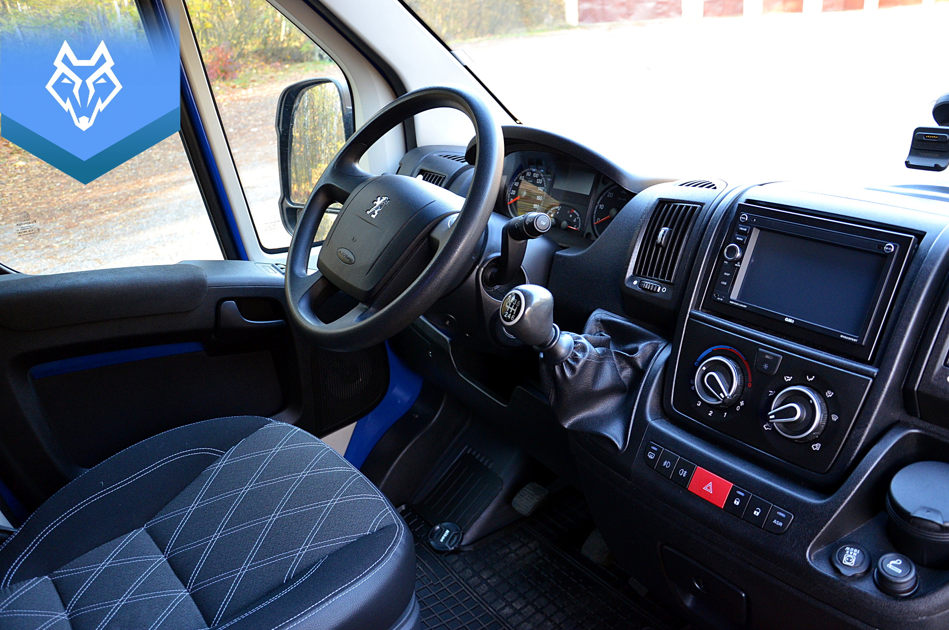 Wnętrze busa Peugeot Boxer VIP z tapicerką w romby, widoczna deska rozdzielcza, kierownica z logo Peugeot i dźwignia zmiany biegów.