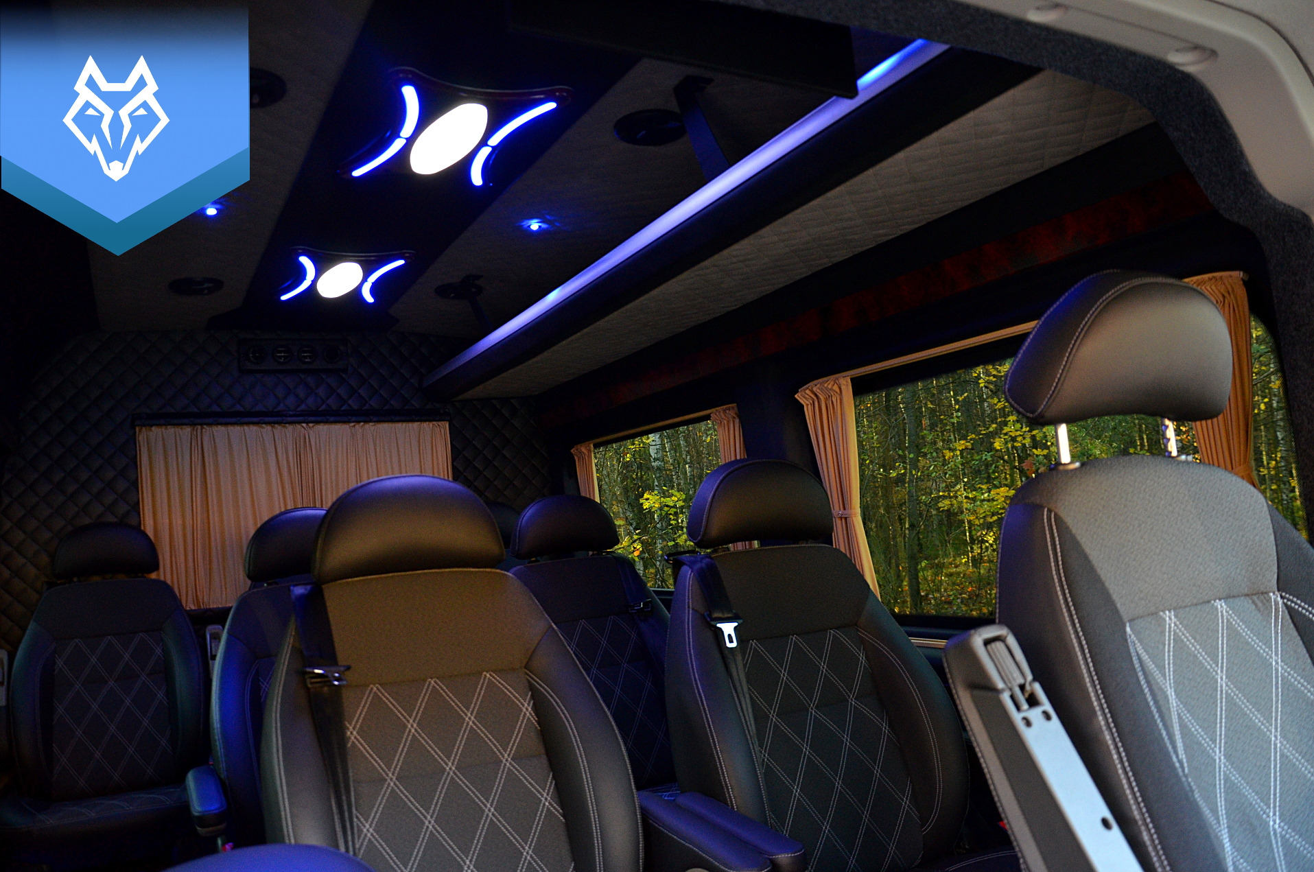 Wnętrze luksusowego busa Peugeot Boxer VIP 8+1 z czarną, pikowaną tapicerką, oświetleniem LED w kolorze niebieskim i widokiem na las za oknem.