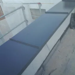 Szczegółowe ujęcie nowo wykonanej, czarnej, metalowej listwy okapowej na krawędzi dachu, z widocznymi elementami rusztowania i zabezpieczeń w tle.