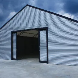 Gotowa hala namiotowa z blachy trapezowej w kolorze srebrnym, z częściowo otwartymi przesuwnymi drzwiami i widoczną konstrukcją wewnętrzną, na betonowej posadzce, z ciemnym, burzowym niebem w tle.