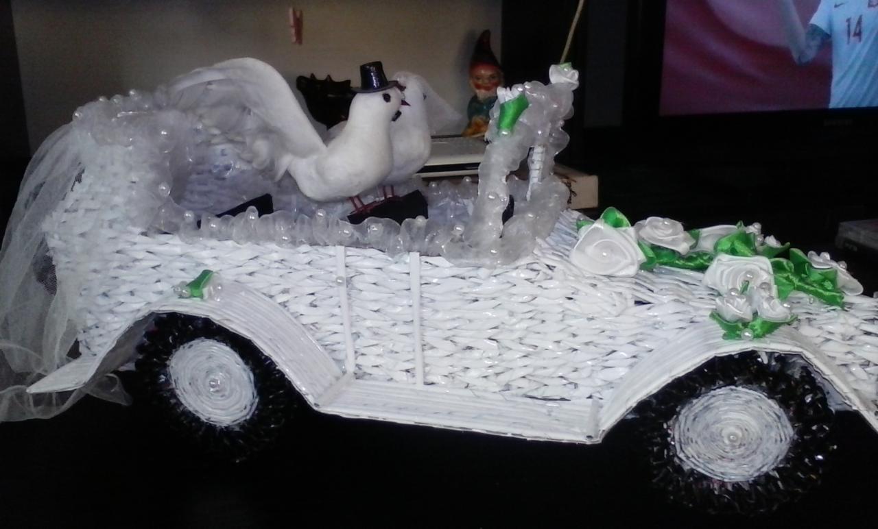 Ręcznie robiony kosz prezentowy w kształcie białego samochodu ślubnego z wikliny, ozdobiony białymi gołębiami w cylindrze, tiulem, sztucznymi różami i figurką krasnala.