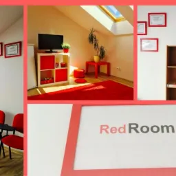 Jasne, przestronne wnętrze sali lekcyjnej z czerwonymi krzesłami, dywanem i akcentami kolorystycznymi, doświetlone oknem dachowym i ozdobione certyfikatami w czerwonych ramkach, z widocznym szyldem...