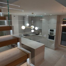 Gallen Sp Zoo - Nowoczesna kuchnia z wyspą i oświetleniem kulistym, widziana z perspektywy drewnianych schodów ze szklaną balustradą.