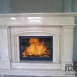 Jasny, marmurowy kominek z płomieniami widocznymi za czarną szybą, logo firmy F.U.H. Floga w prawym dolnym rogu.