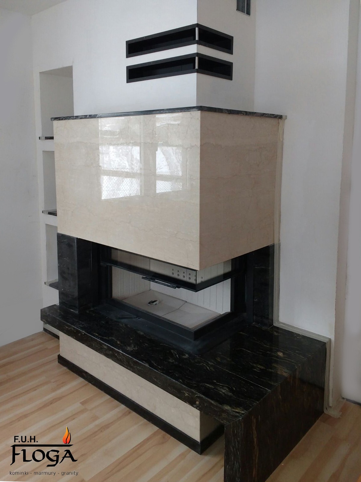 Nowoczesny kominek z obudową z jasnego marmuru i czarnym blatem, wbudowany w ścianę z dekoracyjnymi wnękami.